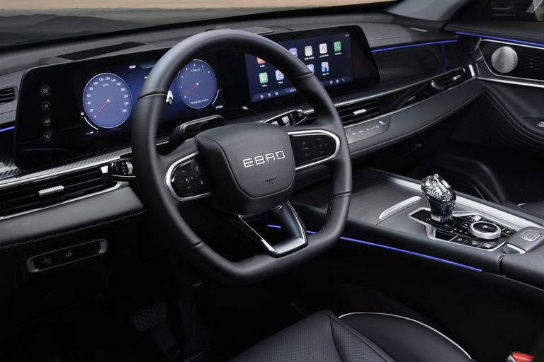 Interior do EBRO s700 PHEV: volante com logótipo EBRO, painel digital duplo e consola central.